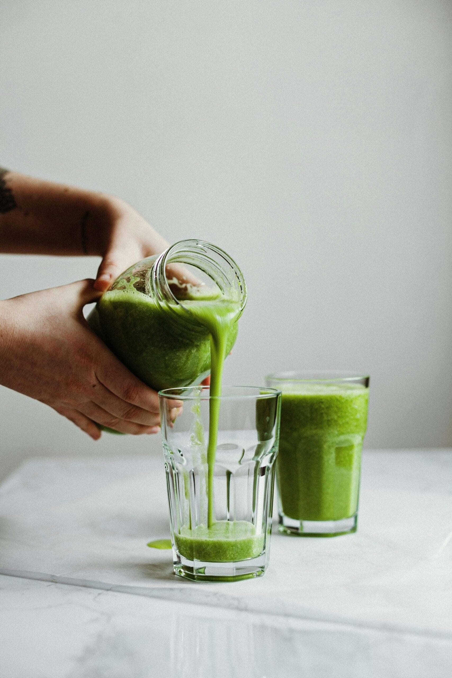 A person pours fresh green celery juice from a mason jar into a glass on a marble countertop. Another glass of celery juice sits nearby. This image represents **celery juicing for health**, highlighting the benefits of **organic, nutrient-rich, anti-inflammatory juice** as discussed in Phillipa Leseberg’s blog. Learn more about **celery juice benefits, digestion support, detox, and holistic wellness at PhillipaLeseberg.com.