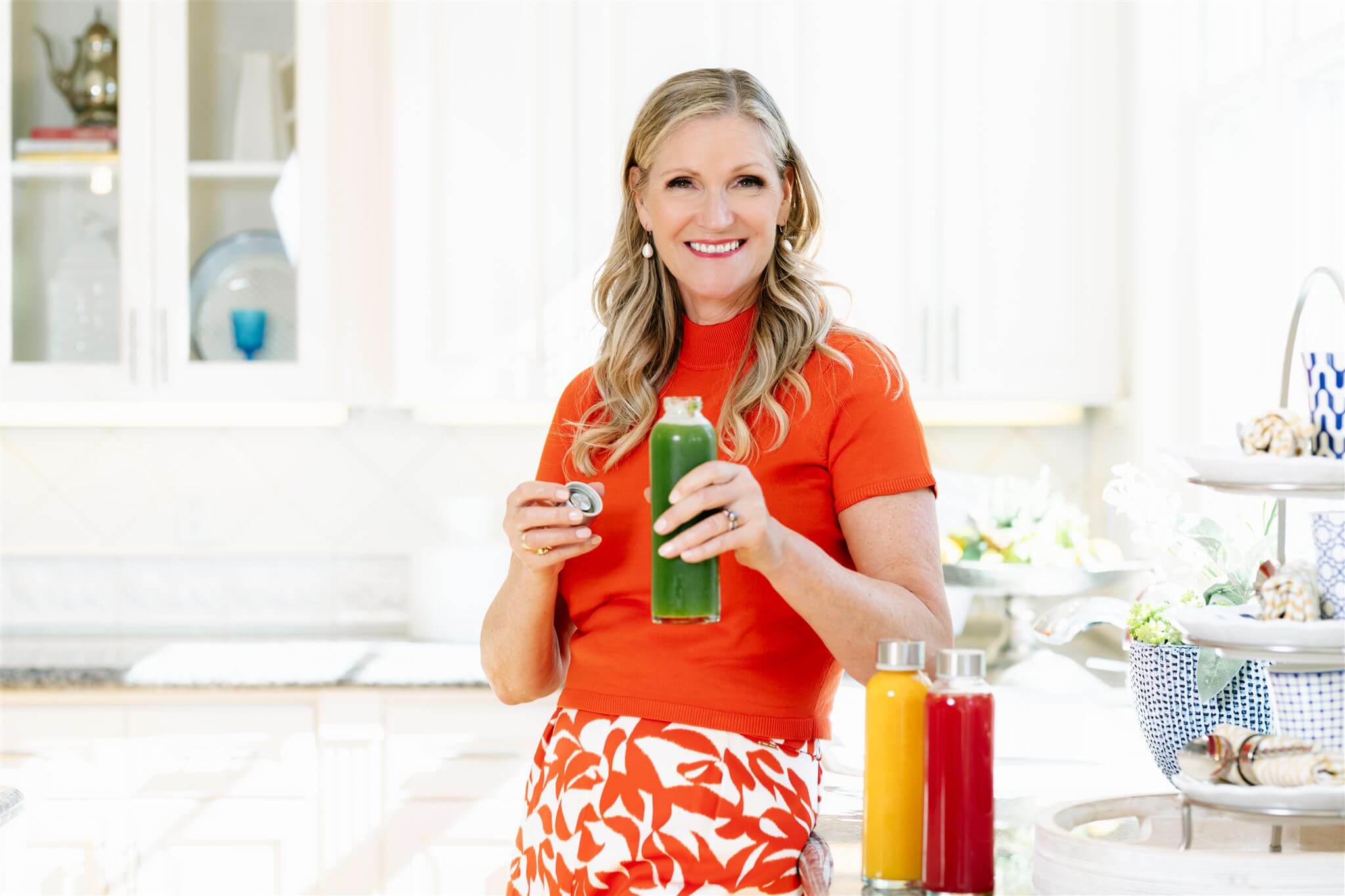 Phillipa Leseberg holding a fresh green juice in a bright kitchen, sharing the benefits of juicing vs. blending. Discover how juicing provides a concentrated nutrient boost, while blending retains fiber for sustained energy. Learn more about organic eating, alternative health, and healing treatments at PhillipaLeseberg.com.